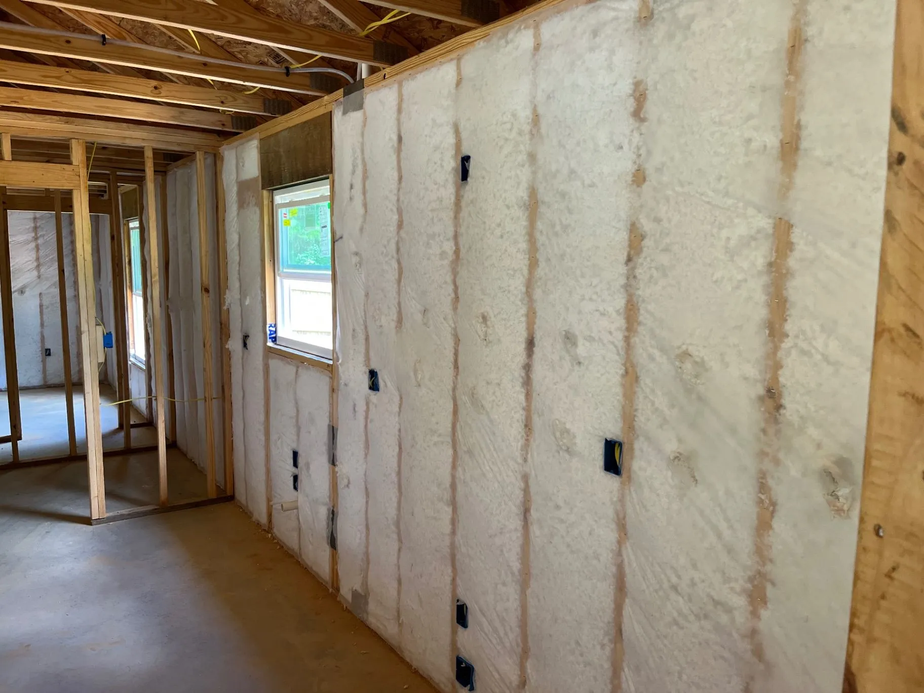 Net-and-blow wall insulation along an open wall with exposed framing and windows