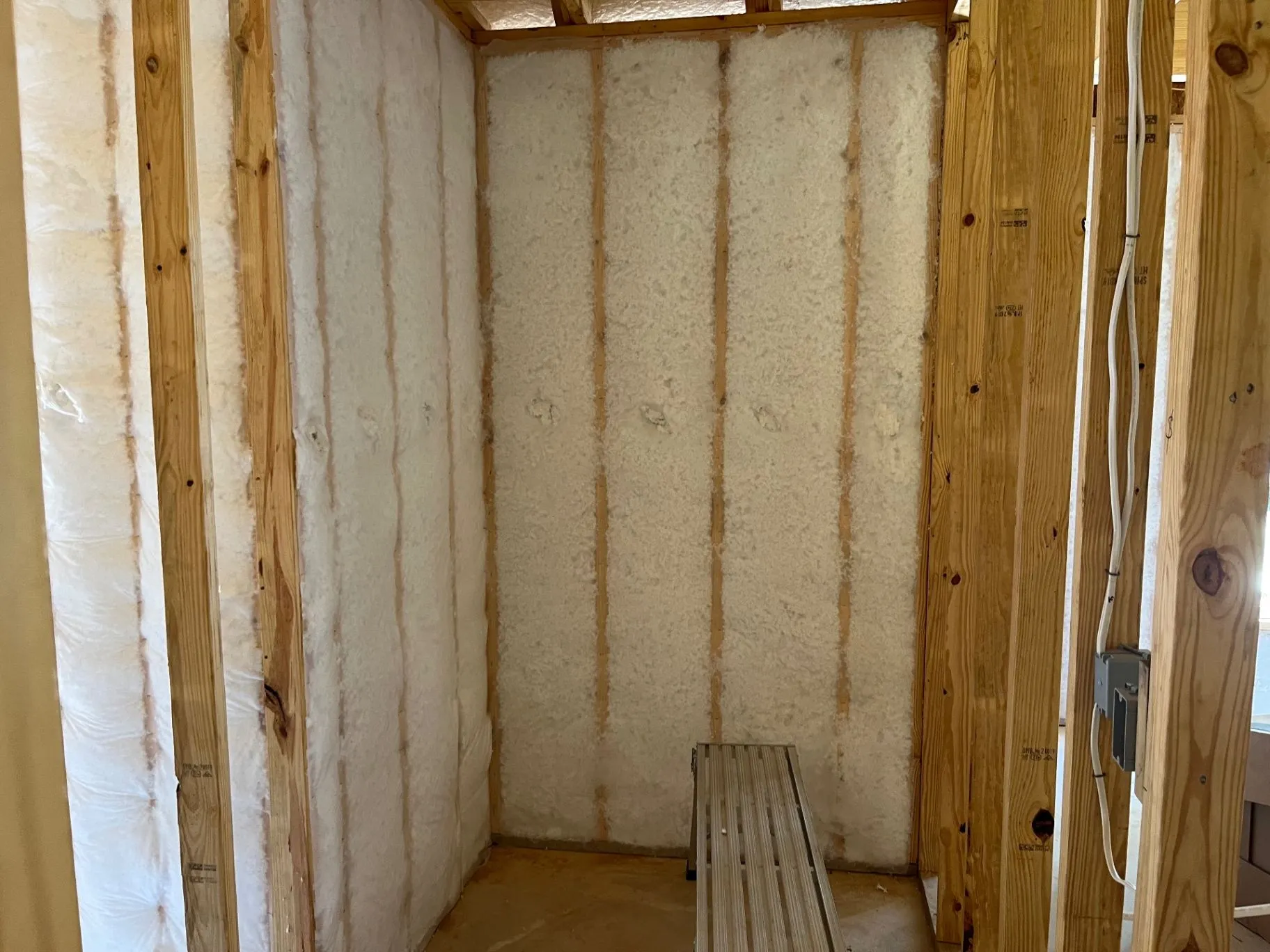 Net-and-blow wall insulation filling open wood-framed wall cavities beneath exposed ceiling framing